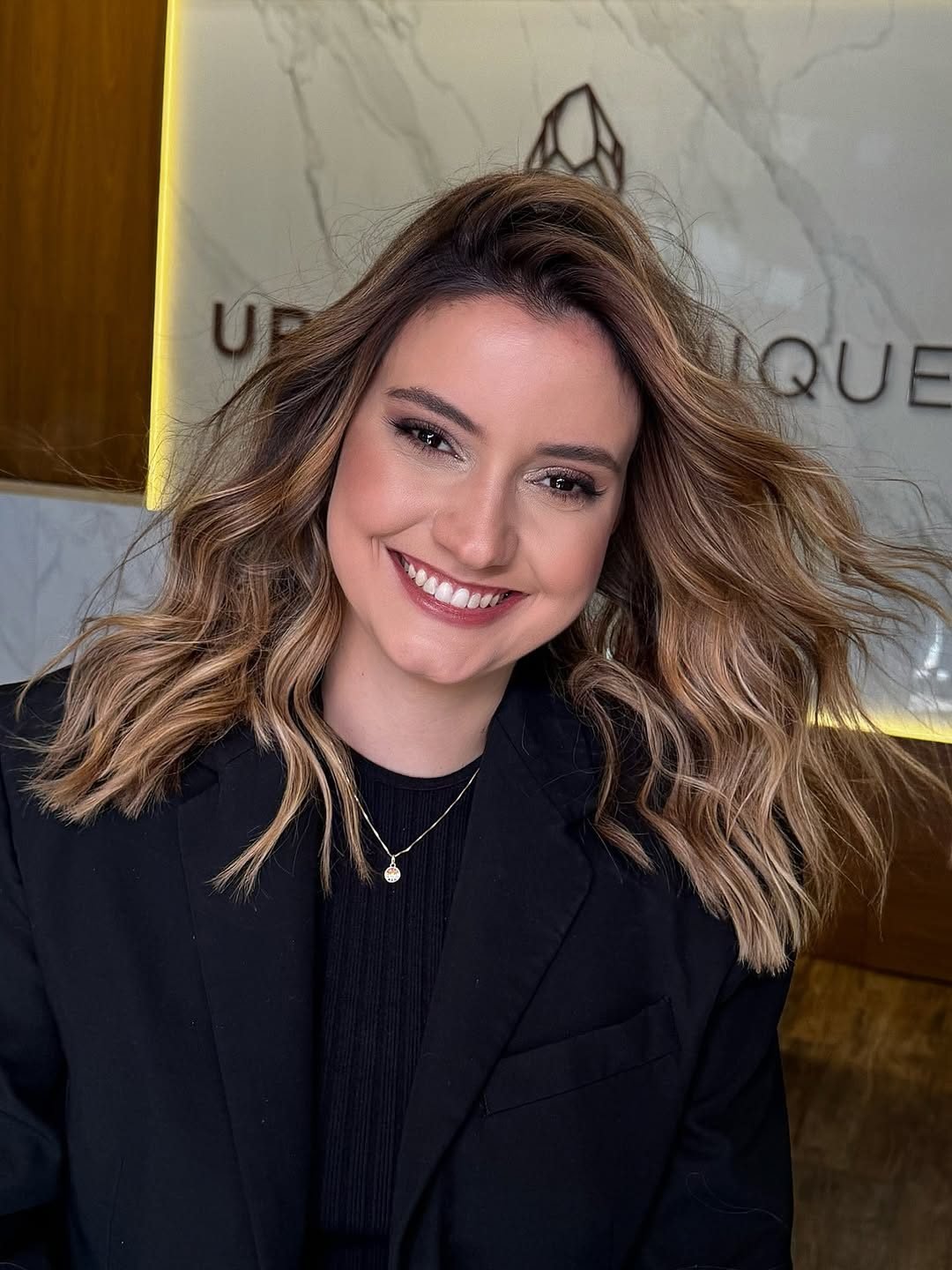 Cliente sorrindo na recepção, com o cristal da Urban Clinique na parede